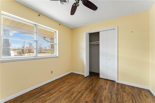 unfurnished bedroom with a textured ceiling, ceiling fan, dark wood-type flooring, and a closet