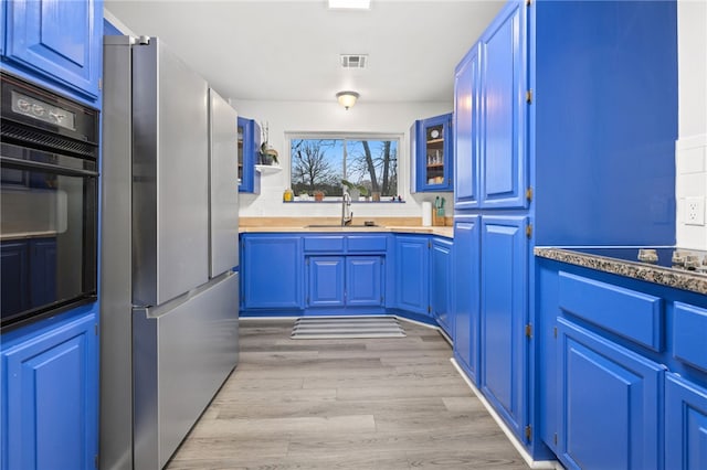 kitchen with blue cabinets, sink, oven, stainless steel fridge, and light wood-type flooring