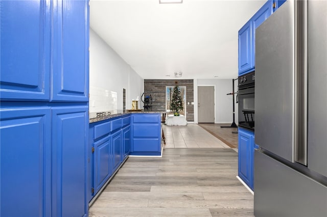 kitchen featuring blue cabinetry, stainless steel refrigerator, oven, light hardwood / wood-style floors, and dark stone counters