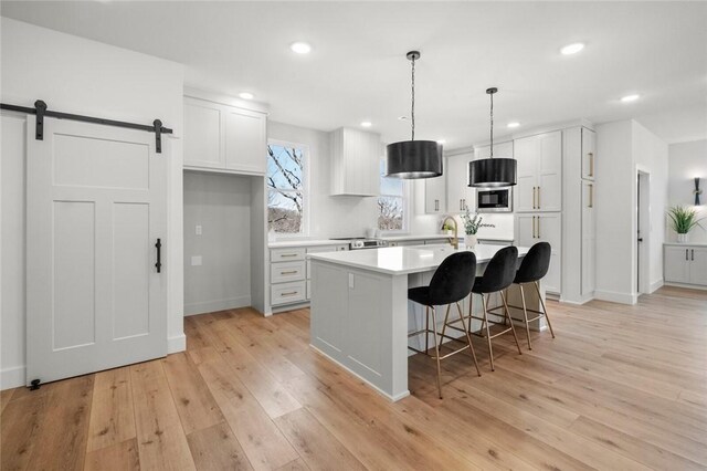 8893 Williams Rd, Rogers, AR 72756 - kitchen with a barn door, light wood-type flooring, white cabinets, a kitchen breakfast bar, and light countertops