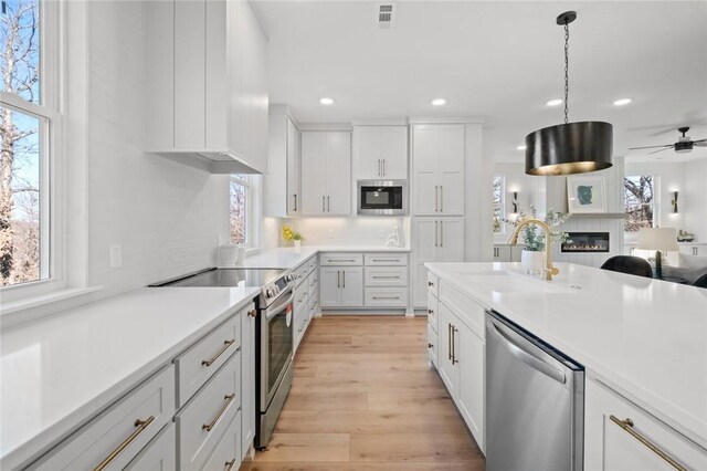 8893 Williams Rd, Rogers, AR 72756 - kitchen featuring stainless steel appliances, healthy amount of natural light, a glass covered fireplace, a ceiling fan, and recessed lighting