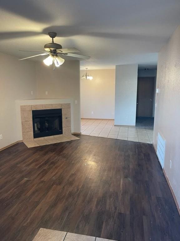 unfurnished living room with a tiled fireplace, hardwood / wood-style floors, and ceiling fan with notable chandelier