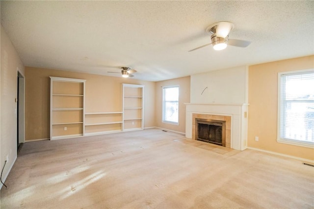 unfurnished living room featuring a tiled fireplace, ceiling fan, plenty of natural light, and a textured ceiling