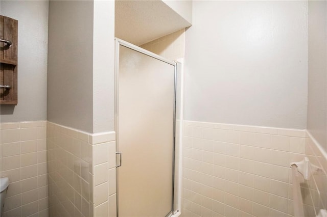 bathroom with a shower with door, tile walls, and toilet