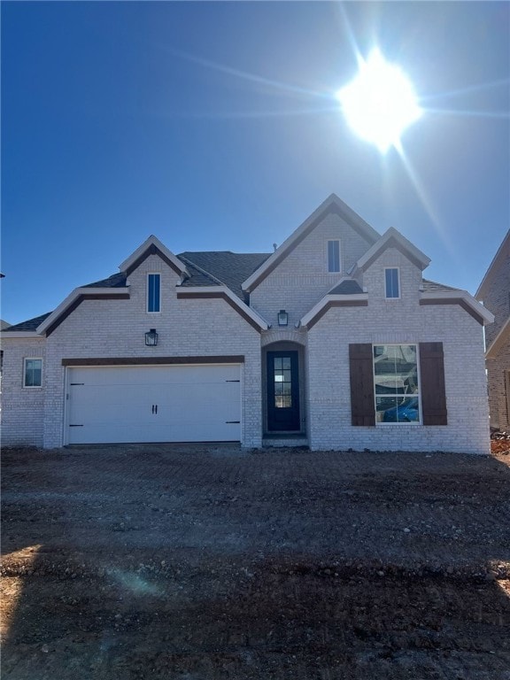 french provincial home featuring a garage, driveway, and brick siding