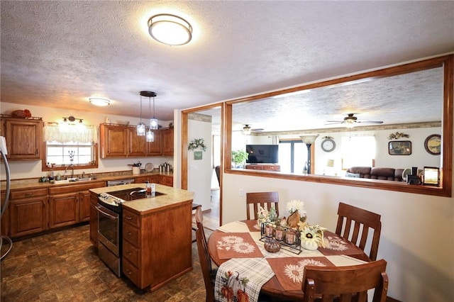 kitchen with sink, stainless steel range with electric stovetop, a center island with sink, pendant lighting, and ceiling fan