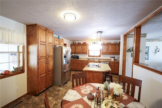 kitchen featuring pendant lighting, sink, appliances with stainless steel finishes, a textured ceiling, and a kitchen island