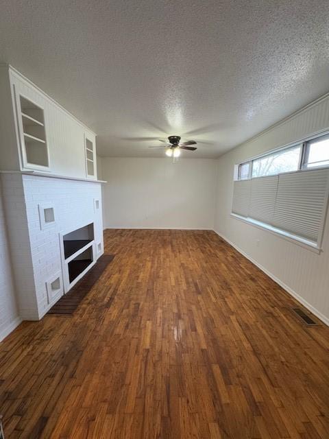 unfurnished living room featuring a textured ceiling, a fireplace, ceiling fan, and dark wood-type flooring