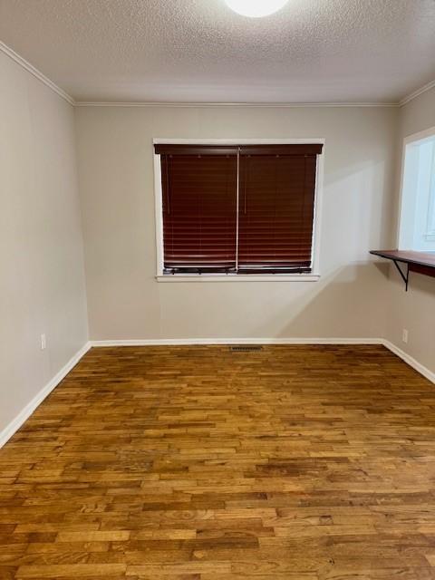 spare room featuring crown molding, wood-type flooring, and a textured ceiling