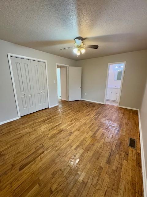 unfurnished bedroom featuring a textured ceiling, ensuite bathroom, light hardwood / wood-style flooring, and ceiling fan