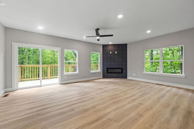 unfurnished living room featuring ceiling fan, a healthy amount of sunlight, and a tiled fireplace