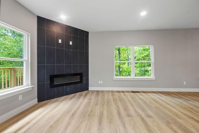 unfurnished living room featuring a tile fireplace, a wealth of natural light, tile walls, and light wood-type flooring