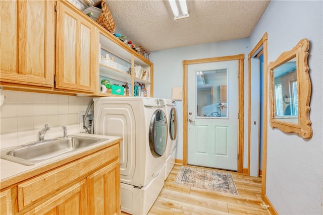 washroom featuring sink, cabinets, light hardwood / wood-style flooring, a textured ceiling, and washer and clothes dryer