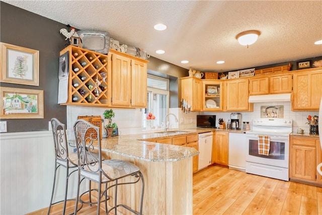 kitchen featuring sink, light stone counters, kitchen peninsula, a textured ceiling, and white appliances