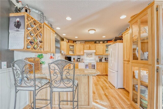 kitchen with a textured ceiling, light brown cabinets, white appliances, and kitchen peninsula