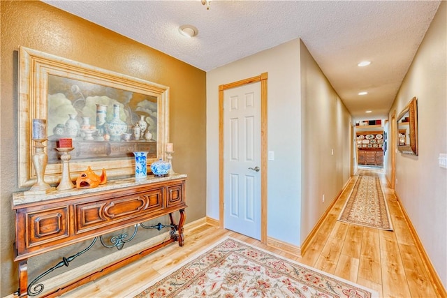 hall with built in features, a textured ceiling, and light wood-type flooring