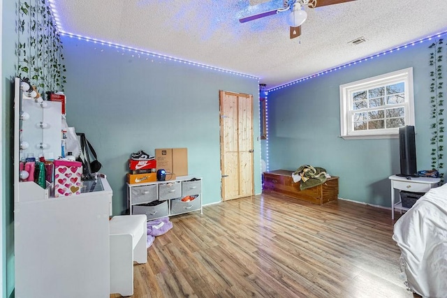 bedroom featuring visible vents, ceiling fan, a textured ceiling, and wood finished floors