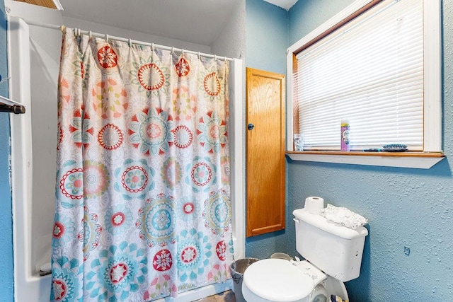 full bath with toilet, a shower with curtain, and a textured wall