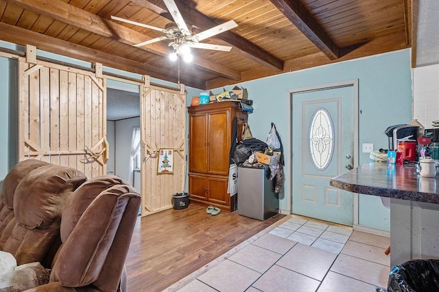 entryway with a barn door, wood ceiling, ceiling fan, light wood-style flooring, and beamed ceiling