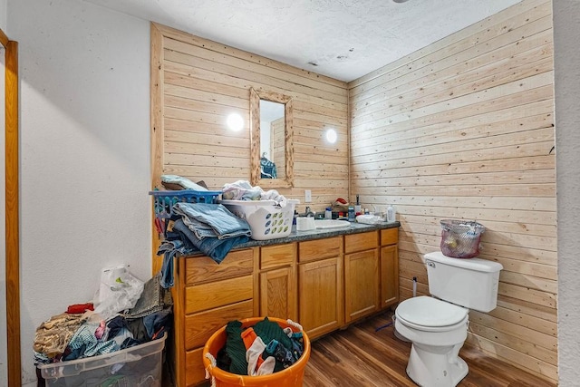 bathroom with hardwood / wood-style floors, vanity, toilet, and wooden walls