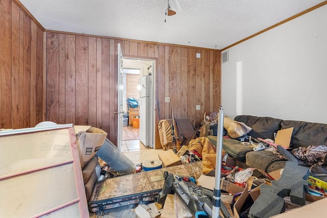 bedroom featuring visible vents, ornamental molding, freestanding refrigerator, wood walls, and a textured ceiling