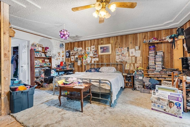 bedroom featuring carpet, ceiling fan, a textured ceiling, and wooden walls