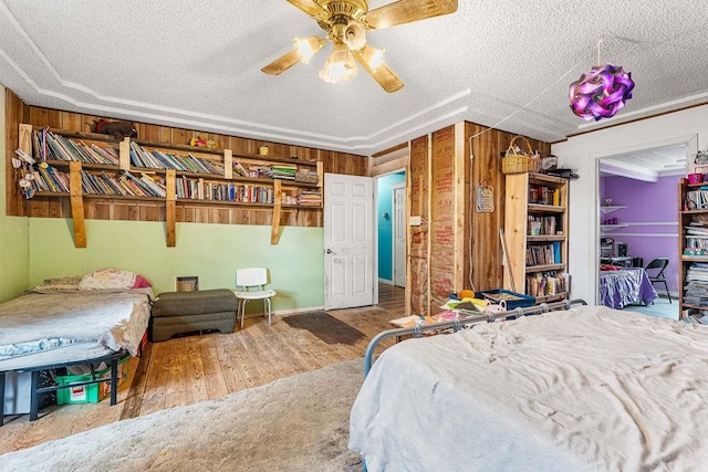 bedroom featuring a textured ceiling, hardwood / wood-style flooring, ceiling fan, and wooden walls