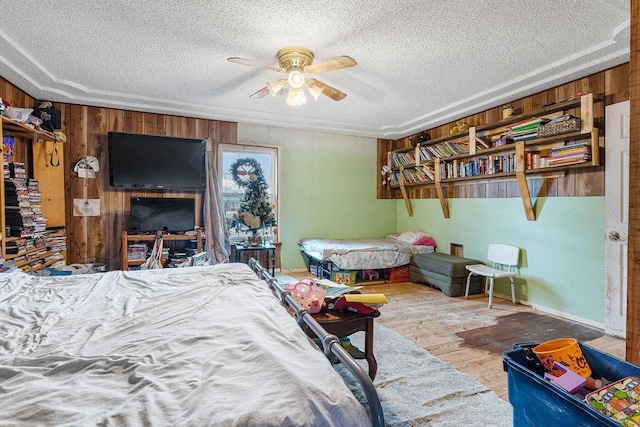 bedroom with ceiling fan, wooden walls, a textured ceiling, and hardwood / wood-style flooring