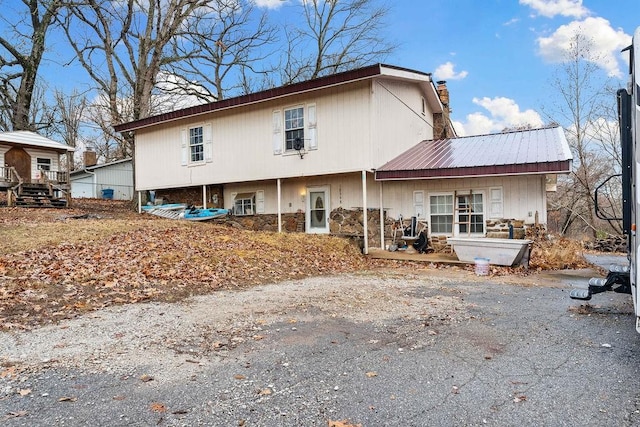 back of property with stone siding, a chimney, and metal roof