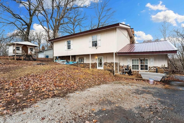 back of house with stone siding, metal roof, and a chimney