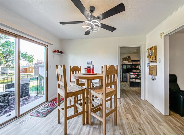 dining area with a textured ceiling, light wood-type flooring, and ceiling fan