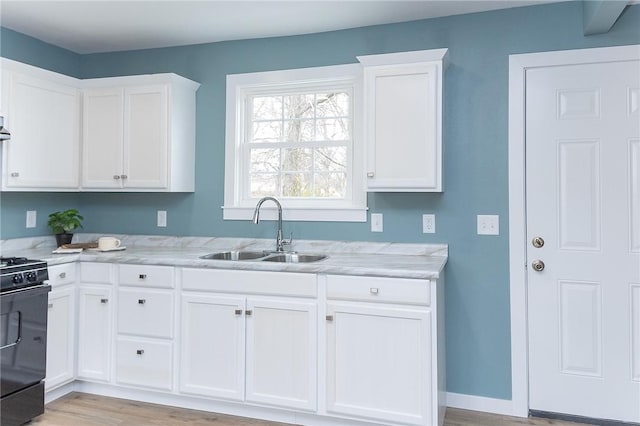 kitchen with white cabinetry, stove, sink, and light hardwood / wood-style flooring