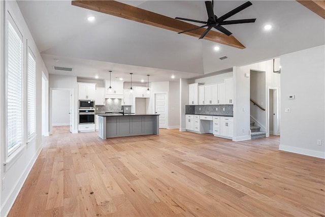 kitchen with white cabinets, stainless steel appliances, beamed ceiling, hanging light fixtures, and an island with sink