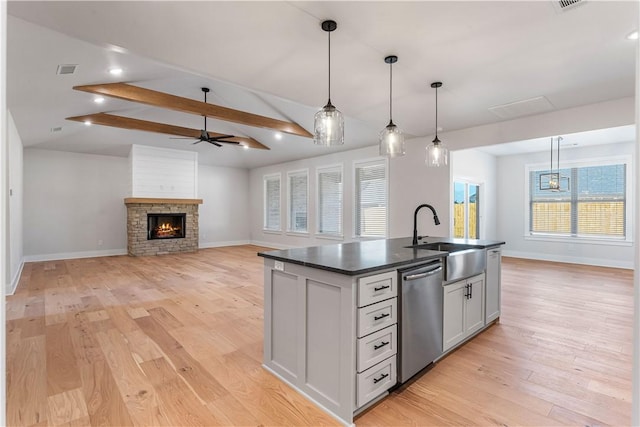 kitchen featuring stainless steel dishwasher, ceiling fan, a kitchen island with sink, sink, and a fireplace