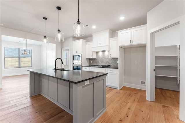 kitchen featuring a kitchen island with sink, pendant lighting, white cabinets, and stainless steel appliances