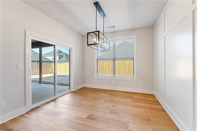 unfurnished dining area featuring light wood-type flooring and a notable chandelier