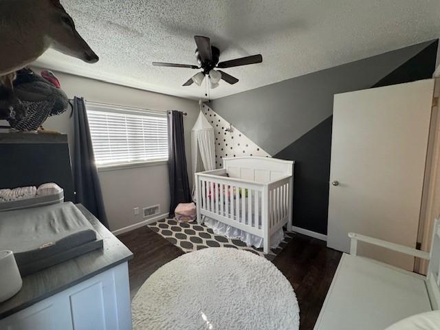 bedroom with a crib, a textured ceiling, dark hardwood / wood-style floors, and ceiling fan