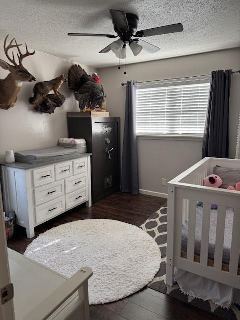 bedroom featuring a textured ceiling, a crib, ceiling fan, and dark hardwood / wood-style floors