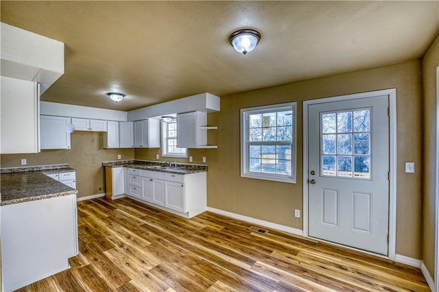 kitchen with white cabinets, dark stone countertops, light wood-type flooring, and sink