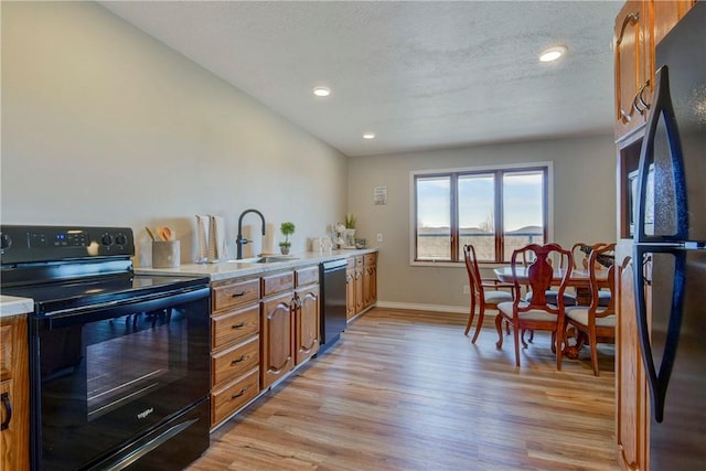 kitchen featuring a textured ceiling, sink, light hardwood / wood-style floors, and black appliances