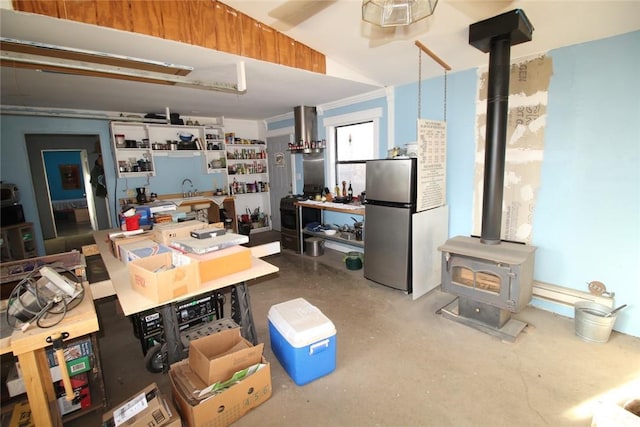 kitchen with concrete flooring, a wood stove, vaulted ceiling, and stainless steel refrigerator