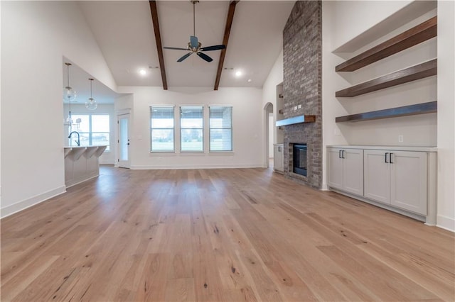 unfurnished living room with high vaulted ceiling, ceiling fan, a fireplace, beamed ceiling, and light hardwood / wood-style floors