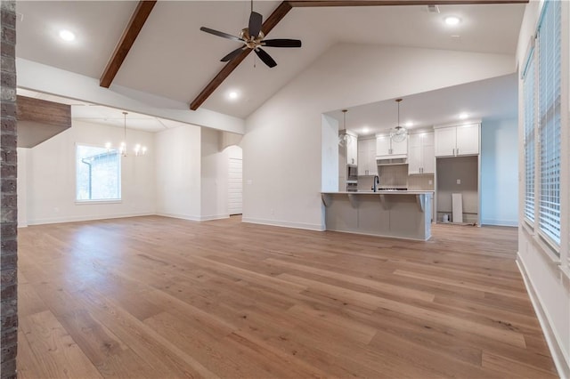 unfurnished living room featuring plenty of natural light, high vaulted ceiling, ceiling fan with notable chandelier, and light hardwood / wood-style flooring