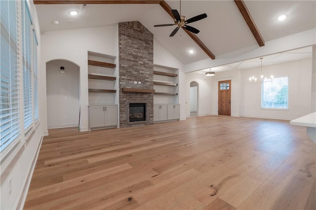 unfurnished living room featuring high vaulted ceiling, ceiling fan with notable chandelier, beam ceiling, a fireplace, and light hardwood / wood-style floors