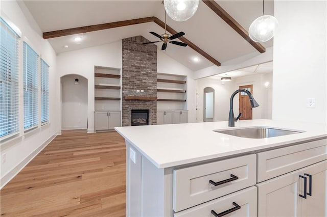 kitchen with vaulted ceiling with beams, decorative light fixtures, white cabinetry, and light hardwood / wood-style flooring