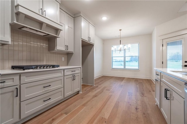 kitchen featuring gas stovetop, backsplash, a chandelier, light hardwood / wood-style floors, and decorative light fixtures