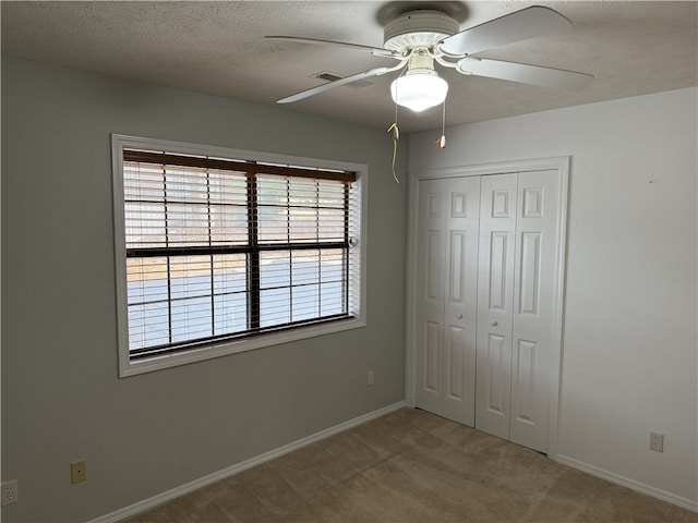 unfurnished bedroom featuring ceiling fan, a closet, light colored carpet, and a textured ceiling