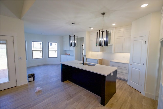 kitchen featuring sink, decorative light fixtures, light hardwood / wood-style flooring, white cabinets, and an island with sink