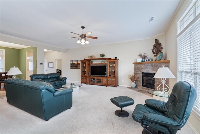 carpeted living room with ceiling fan, a stone fireplace, ornamental molding, and a wealth of natural light