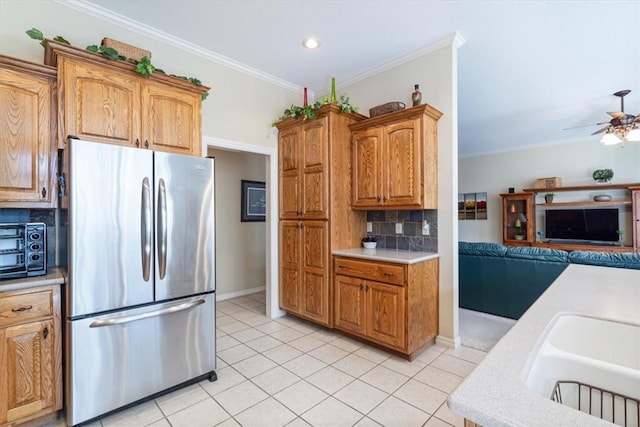 kitchen featuring decorative backsplash, ornamental molding, ceiling fan, stainless steel refrigerator, and light tile patterned flooring